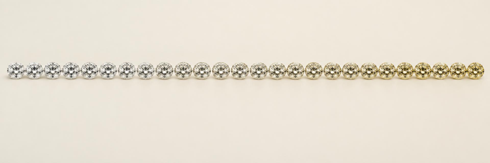 Twenty-three round brilliant diamonds under consistent lighting, progressing gradually from colorless D toward visibly warmer Z
